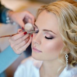 Wedding makeup artist making a make up for bride. Beautiful sexy model girl indoors. Beauty woman with curly hair. Female portrait. Bridal morning of a cute lady. Close-up hands near face