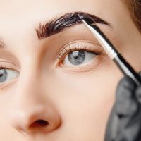 Master brush dye henna eyebrows woman in beauty salon. Correction of brow hair.